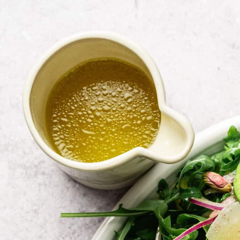 Dijon maple vinaigrette in a white carafe next to a salad.