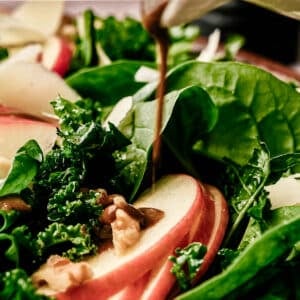 Balsamic basil salad dressing being drizzled on top of a kale and spinach salad.