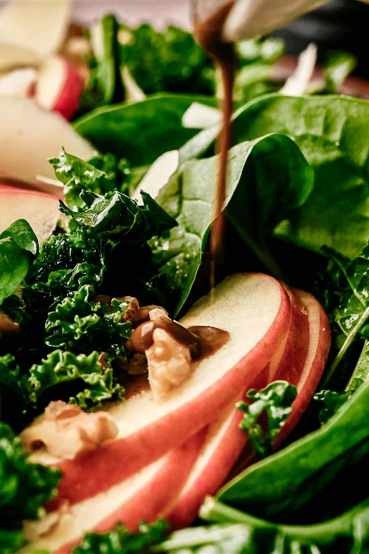 Balsamic basil salad dressing being drizzled on top of a kale and spinach salad.