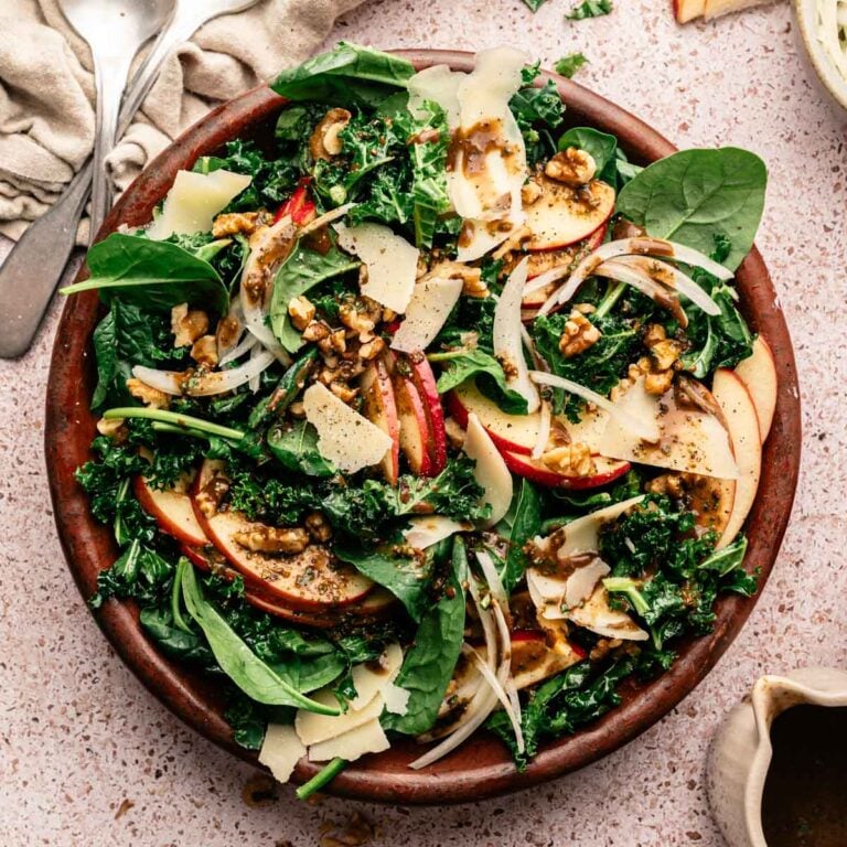 Spinach and kale salad with sliced apples, vegan parm, onion, and more.