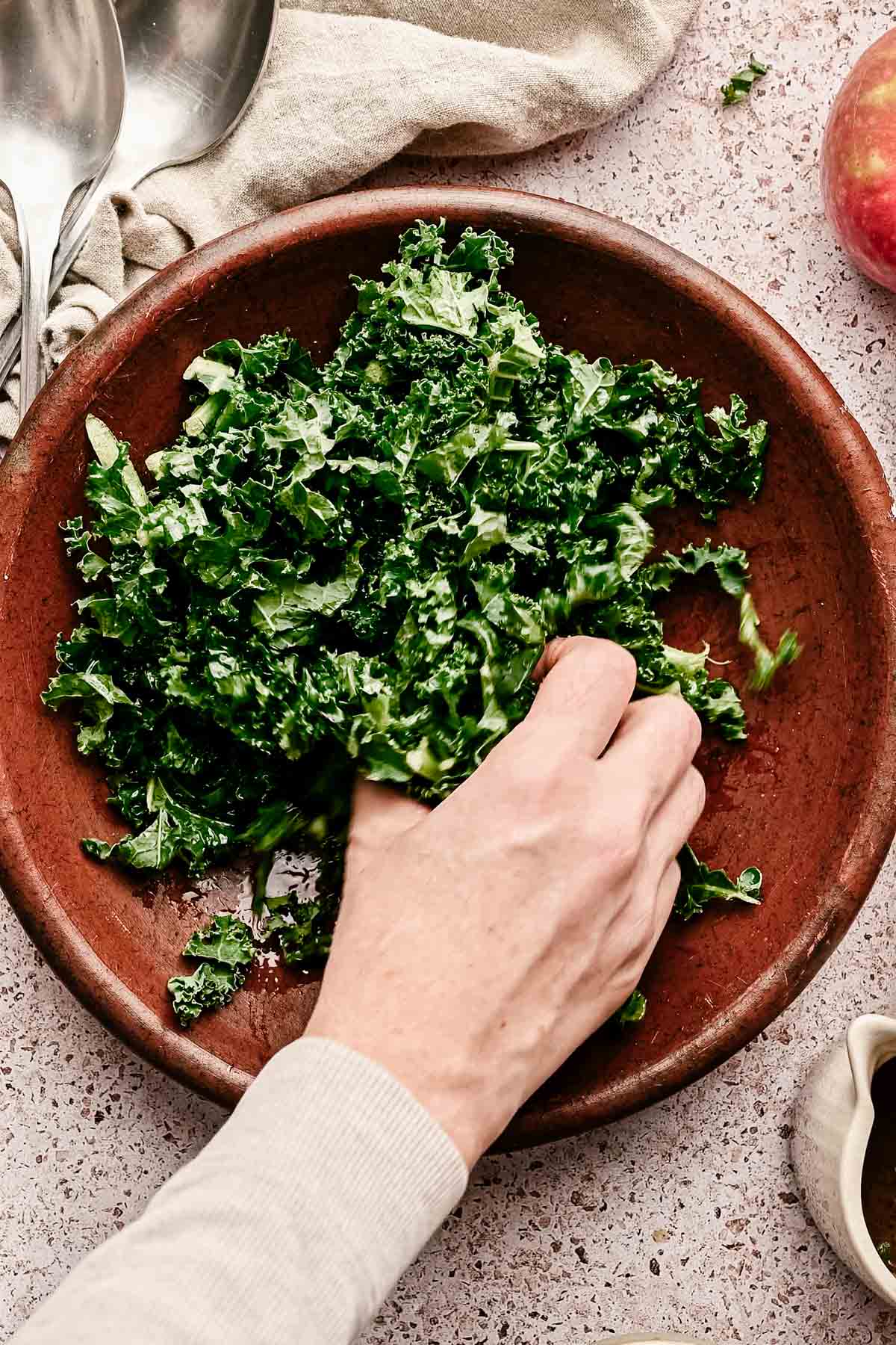 Massaging kale in a terracotta colored shallow bowl.