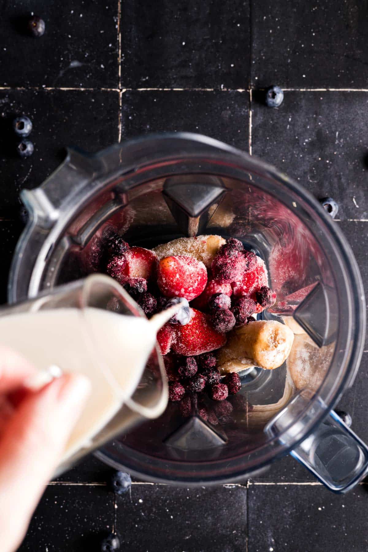 Milk being poured into a blender full of frozen fruit.